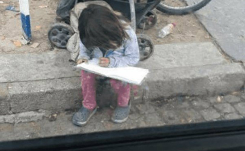 La niña hace la tarea en la calle, mientras espera por el semáforo para volver a pedir. 